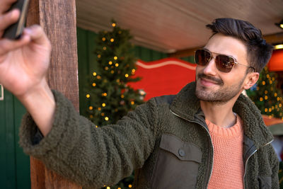 Young man wearing sunglasses while standing against christmas tree