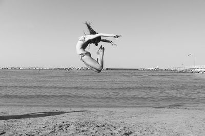 Young woman jumping at beach against clear sky