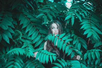 Young woman looking away while standing amidst plants