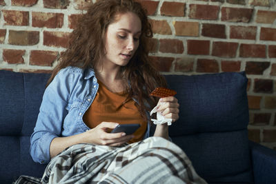 Young woman using mobile phone while sitting on sofa at home