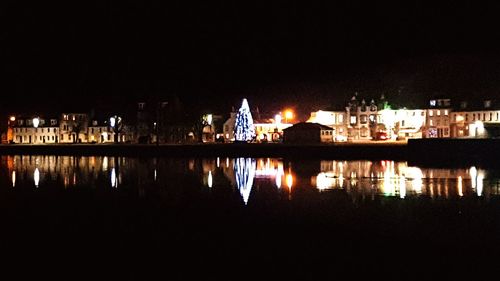 Illuminated buildings by lake against clear sky at night