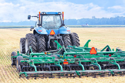 An agricultural tractor with a hitch harrow, stands against the background of harvested wheat field.