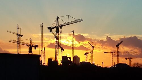 Silhouette cranes against sky at sunset