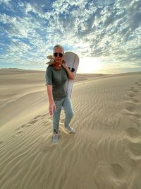 Full length of woman holding sandboard at desert during sunset