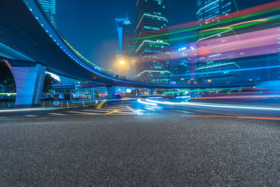 Light trails on road by illuminated buildings in city at night