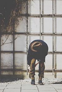 Full length of man adjusting jeans on footpath against wall