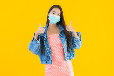 Portrait of young woman standing against yellow background