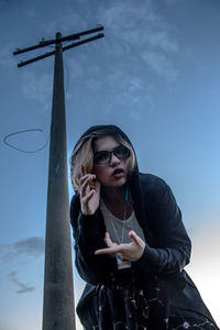 Low angle view of young woman using mobile phone against sky