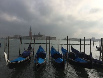 Gondola moored on canal with san giorgio maggiore in background against cloudy sky