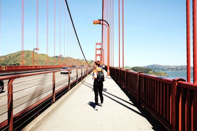 Rear view of woman walking on golden gate bridge against blue sky