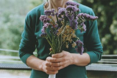 Midsection of woman holding purple flowers while standing by railing