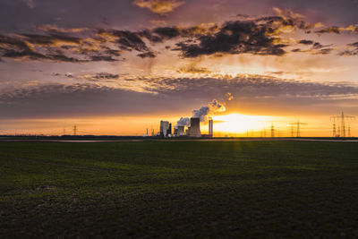 Distant view of factory against cloudy sky during sunset