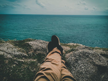 Low section of man relaxing on rock formation by sea