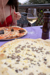 Midsection of women eating pizza with wine on table at restaurant 