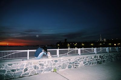 Rear view of woman sitting against illuminated building at night