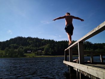 Full length of shirtless man jumping in lake against sky