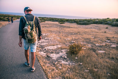 Rear view of man walking on road by field against sky