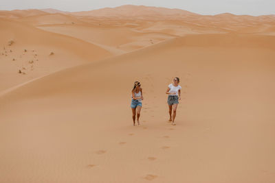 Rear view of friends walking on sand dune