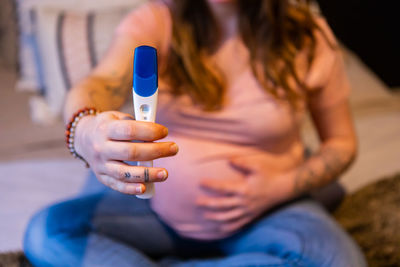 Midsection of pregnant woman holding pregnancy test kit at home