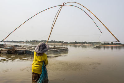 Rear view of man fishing in river against clear sky