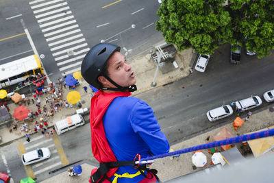 Man dressed as a superhero rappelling down from a tall building. 
