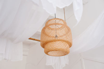 A stylish wicker wooden chandelier in boho and bali style hangs on the ceiling 