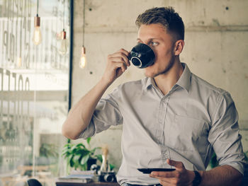 Young man looking away while drinking coffee cup