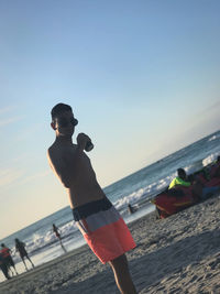 Full length of shirtless man on beach against clear sky