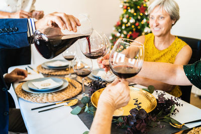 Cheerful friends and family members gathering together at table and holding glasses with red wine during christmas dinner
