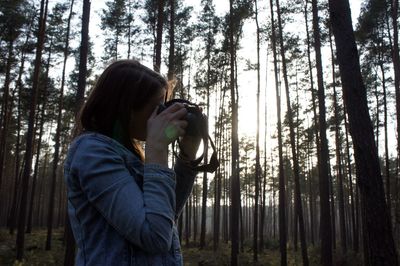 Side view of woman photographing through camera at forest