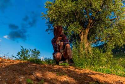 Full length of woman sitting by tree against sky