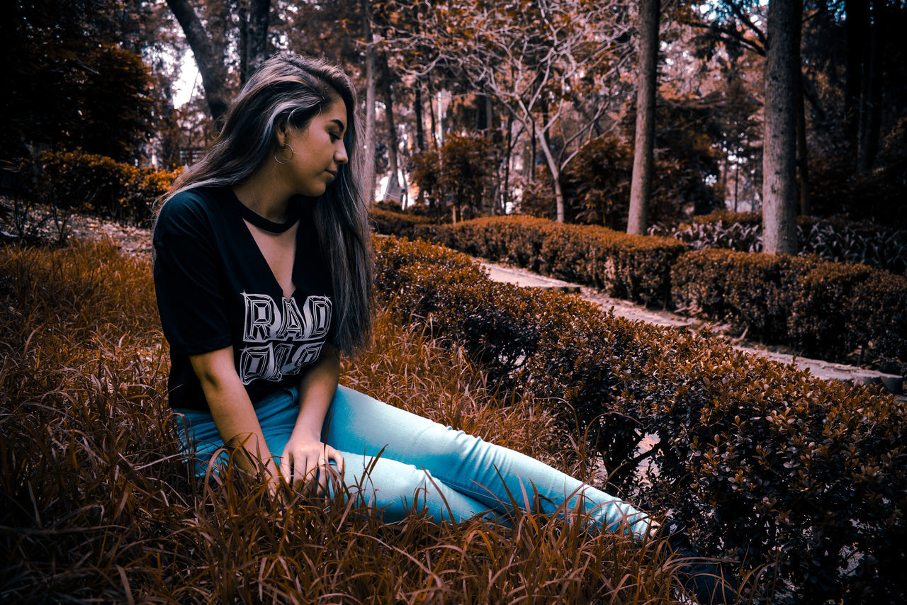 YOUNG WOMAN LOOKING AWAY WHILE STANDING ON LAND