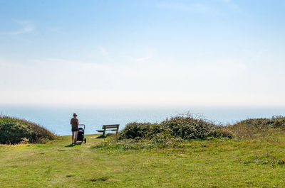 Man sitting on grass by sea against sky