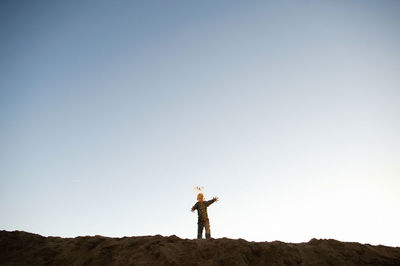 Boy playing with sand while standing at beach against sky