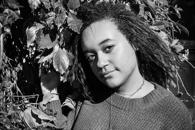 Portrait of young woman with leaves against trees