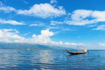 Fisherman rowing boat in sea against sky