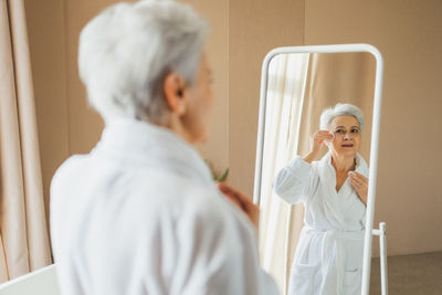 Side view of woman using mobile phone while sitting on bed at home
