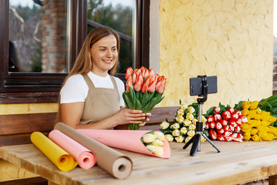 A young female florist packs bouquets of tulips in her shop and shoots a video master class 