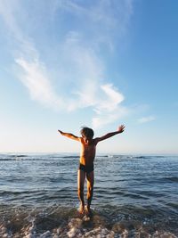 Full length of woman with arms raised on beach against sky