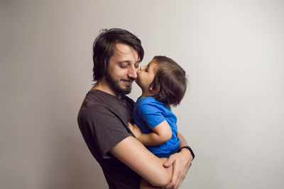 Father in the gray shirt holding a son in a blue t-shirt in the hands of a white wall