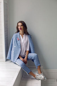 Business woman in a blue suit sits at the big window in the white room