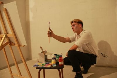 Man holding paintbrush crouching against wall