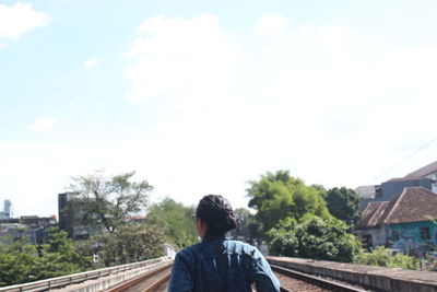 Rear view of man standing by house against sky