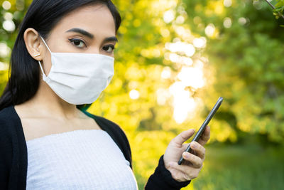 Close-up portrait of young woman holding smart phone outdoors