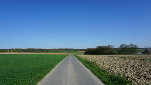 Empty road amidst agricultural field against blue sky