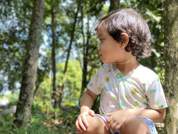 Girl looking away while sitting on tree in forest