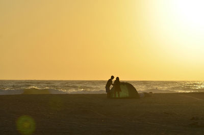 Men on beach against sky during sunset