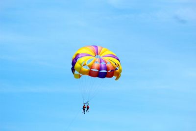 Low angle view of people parasailing against sky