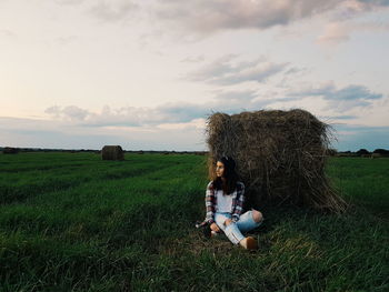 Young woman sitting on grassy field during sunset