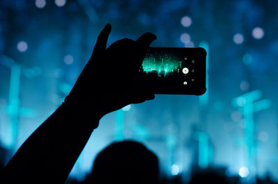 Silhouette hand photographing illuminated smart phone at night